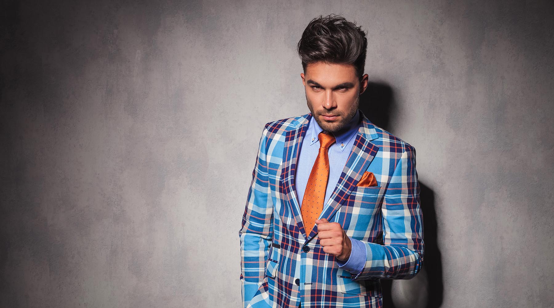 handsome young man wearing orange tie and pocket square with teal white and orange plaid suit
